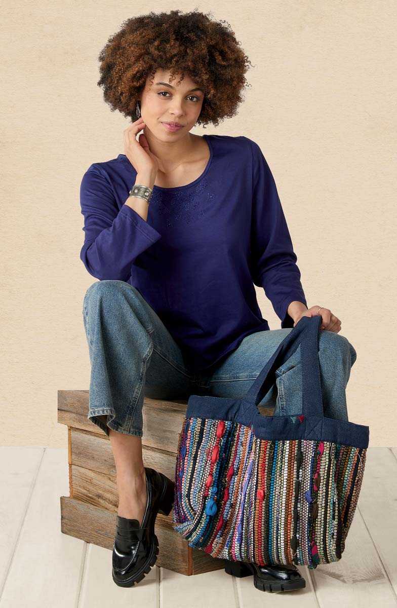Woman sitting on a wooden block holding a colorful bag against a beige background