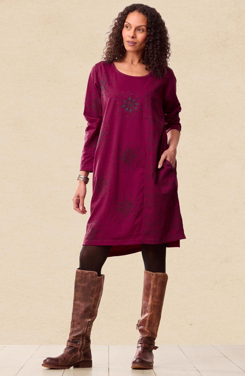Woman wearing a long burgundy dress with a floral pattern and brown knee-high boots on a beige background