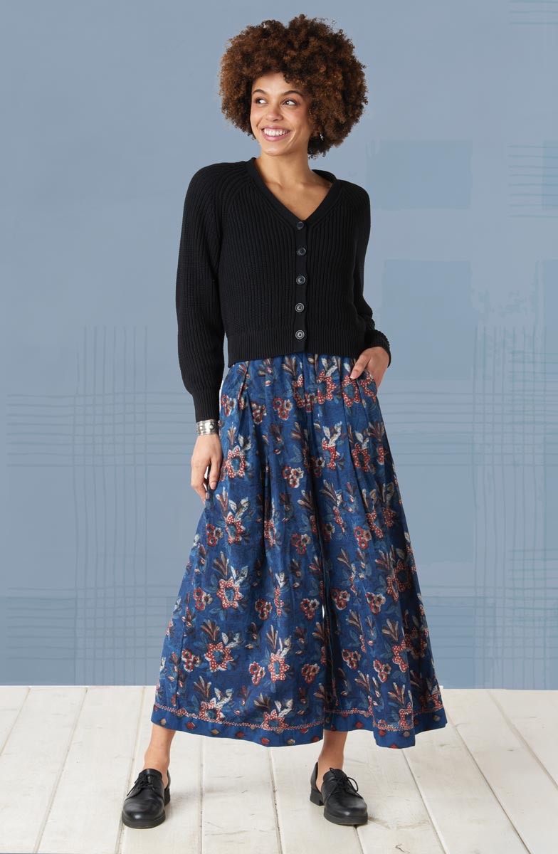 Woman wearing a black cardigan and blue floral skirt against a light blue wall.