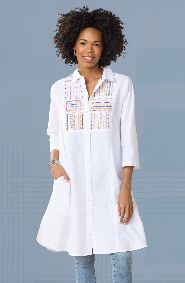 Woman wearing a white embroidered shirt against a gray background