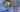A deadstock styled flat-lay of multiple patterned fabric garments and accessories, including a blue patterned top with embroidered motifs, a yellow hanger, and several patterned fabric pieces in purple, blue, and orange tones.