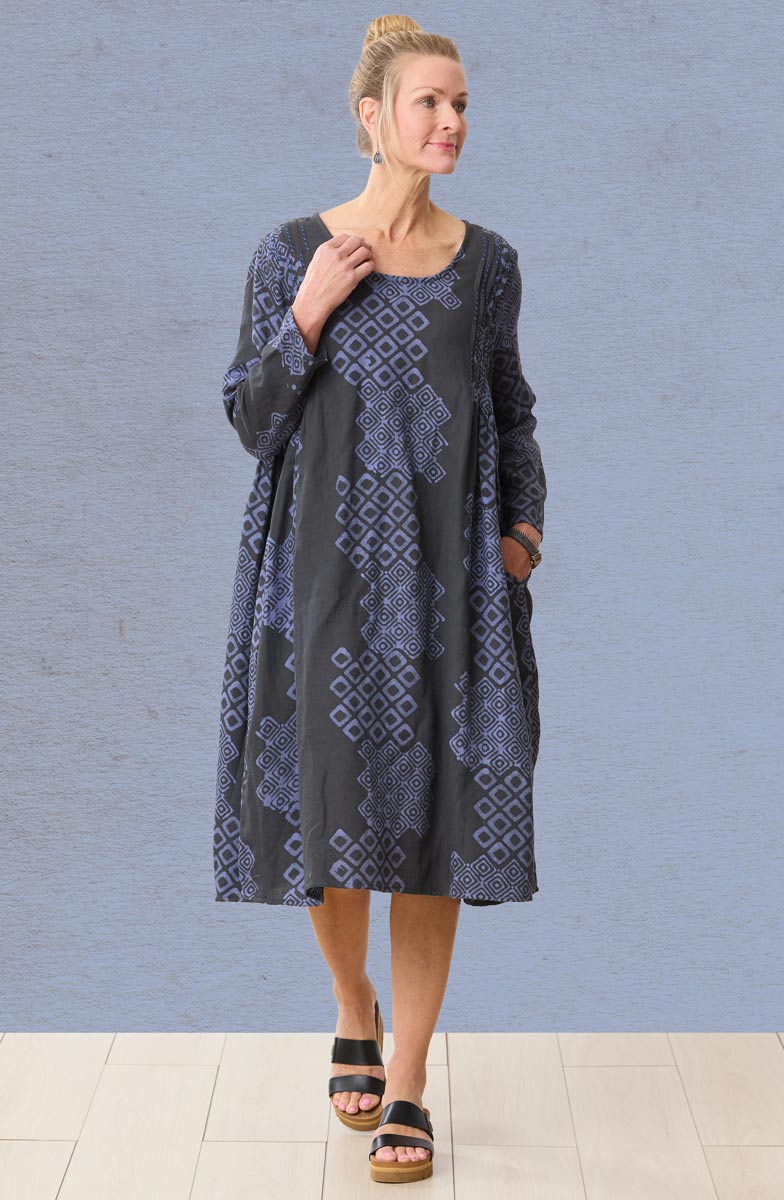 Woman wearing a patterned dress against a blue brick wall.