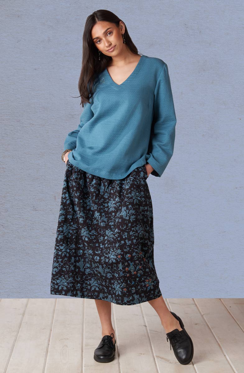 Woman wearing a teal sweater and floral skirt against a gray background