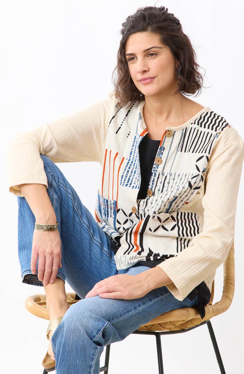 Woman sitting on a chair wearing a patterned top and jeans against a white background