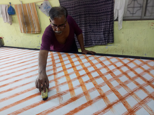 Artisan using a scrub brush to create a unique painted line on fabric.