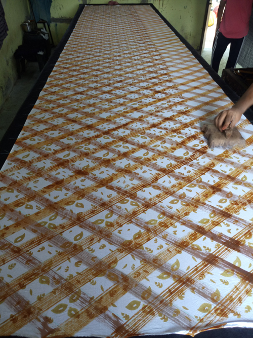 Artisan using scrub brush and paint to create a diagonal checkered pattern on cloth.