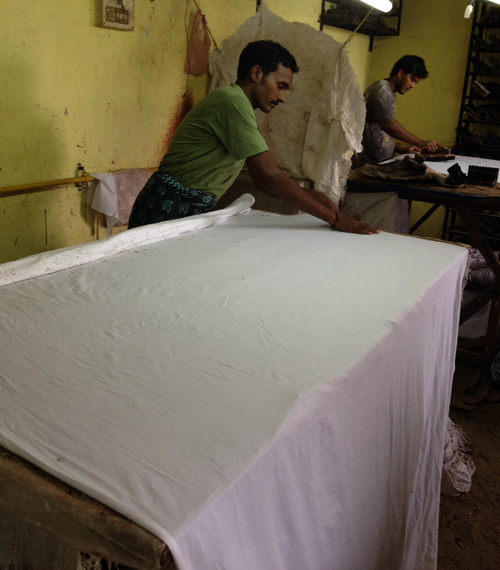 Artisan spreads fabric across a table in preparation for the application of wax.